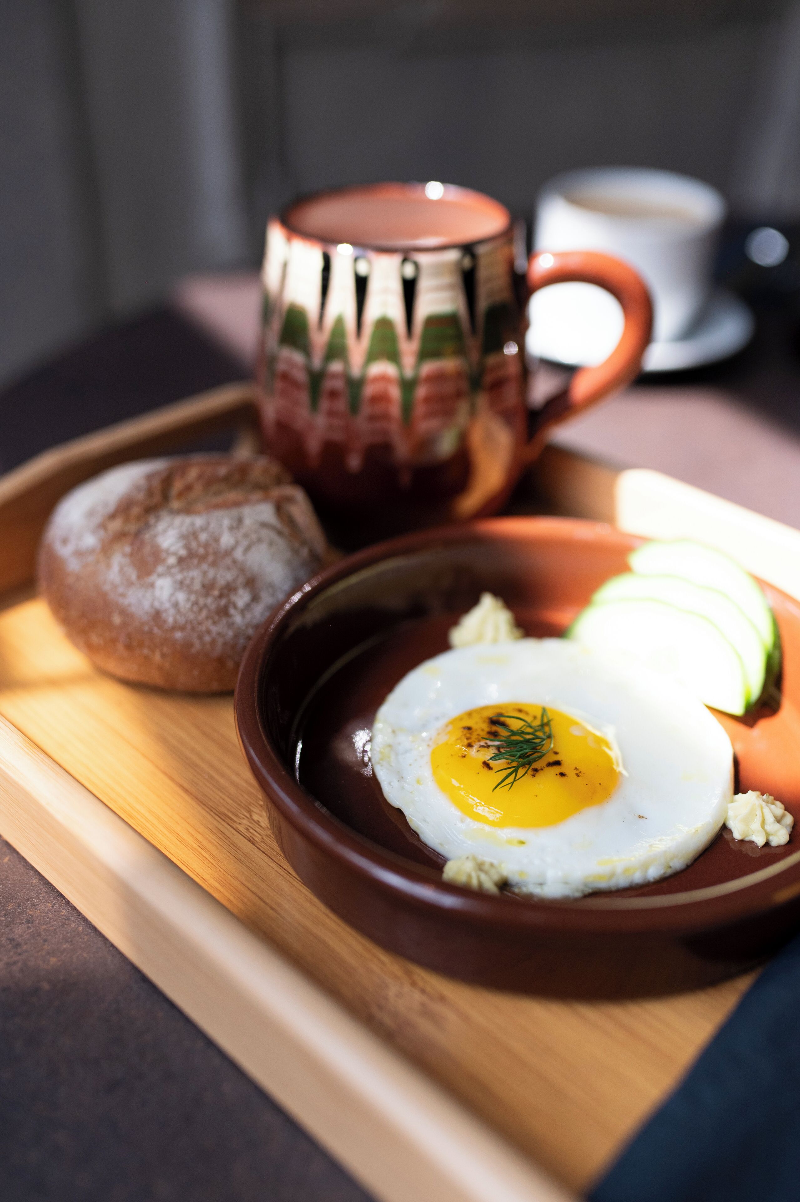 Un plateau de petit-déjeuner avec un pain, des légumes coupés en tranches, un œuf au plat et une tasse.