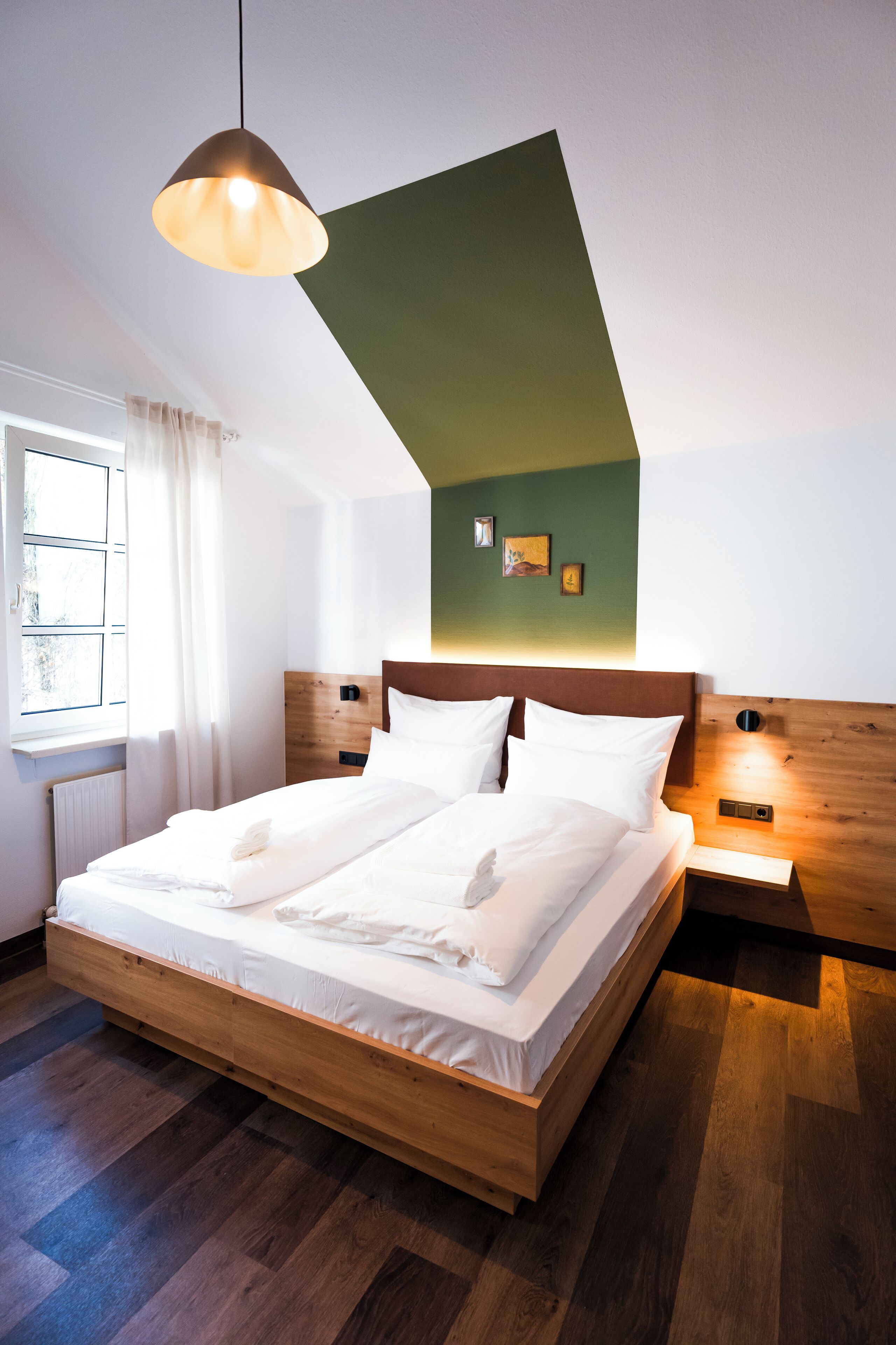 Un dormitorio moderno con una cama de madera, una pared de acento verde y una lámpara colgante.