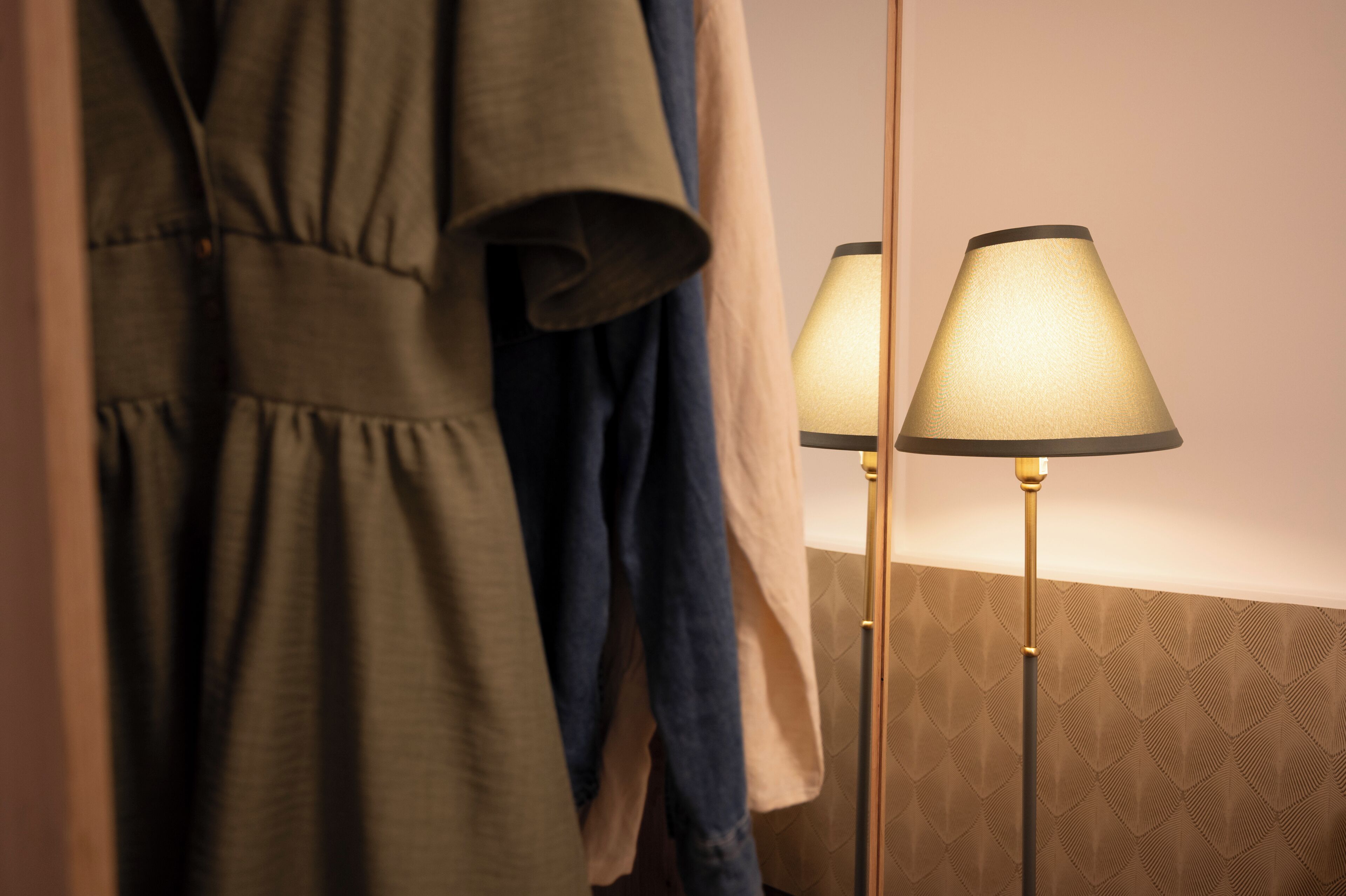 Une pièce avec un miroir reflétant une robe verte et un chemisier beige, ainsi que deux lampadaires avec des abat-jour.