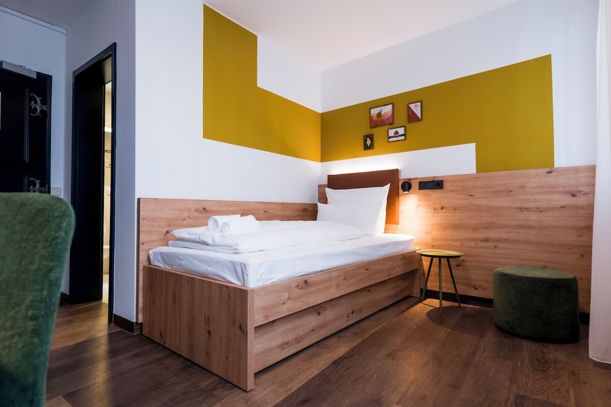 Un dormitorio moderno con una cama de madera, un taburete pequeño y un otoman verde.