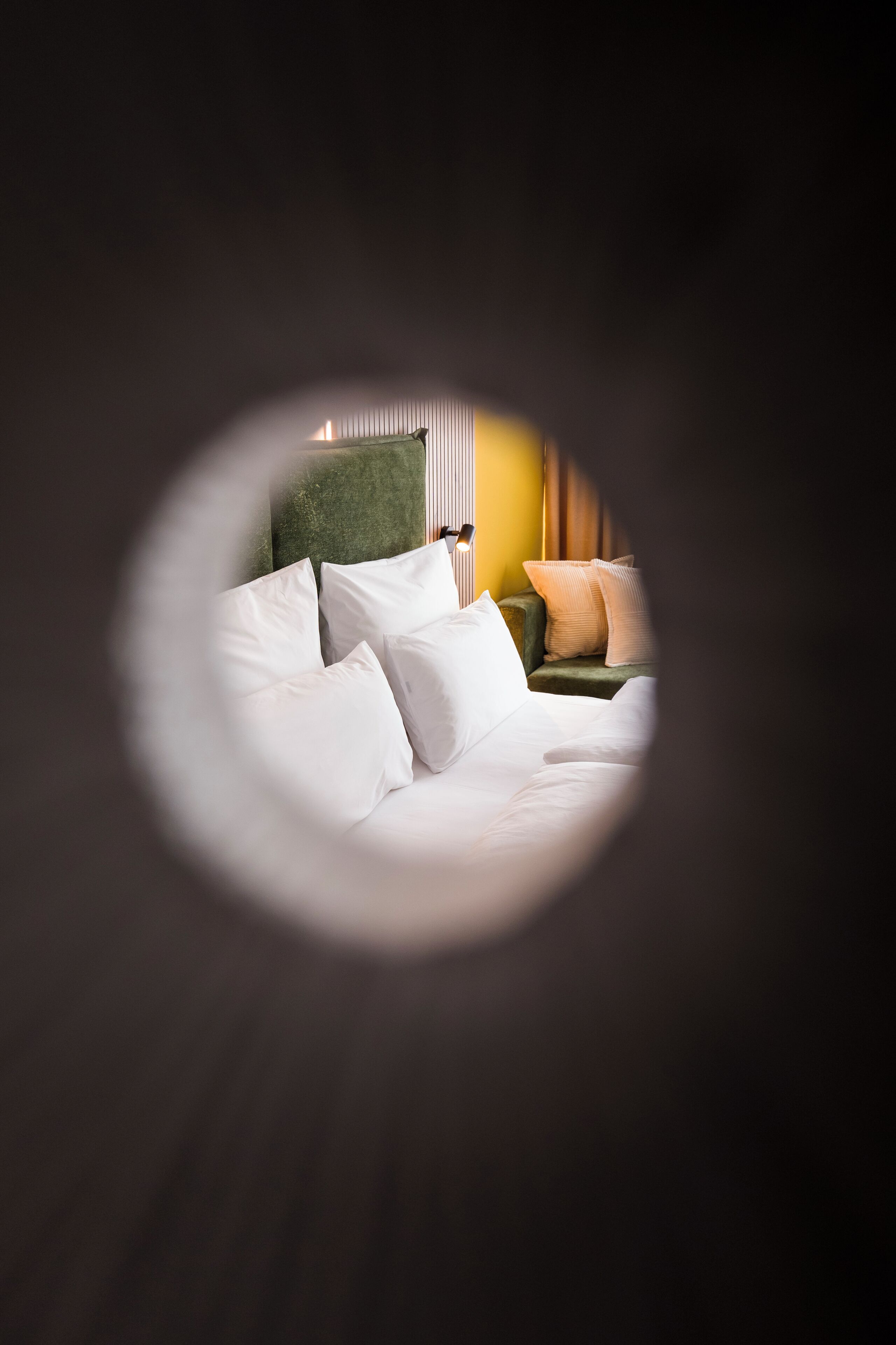 Une chambre d’hôtel avec un lit, des oreillers, une tête de lit verte et une table de chevet avec une lampe.