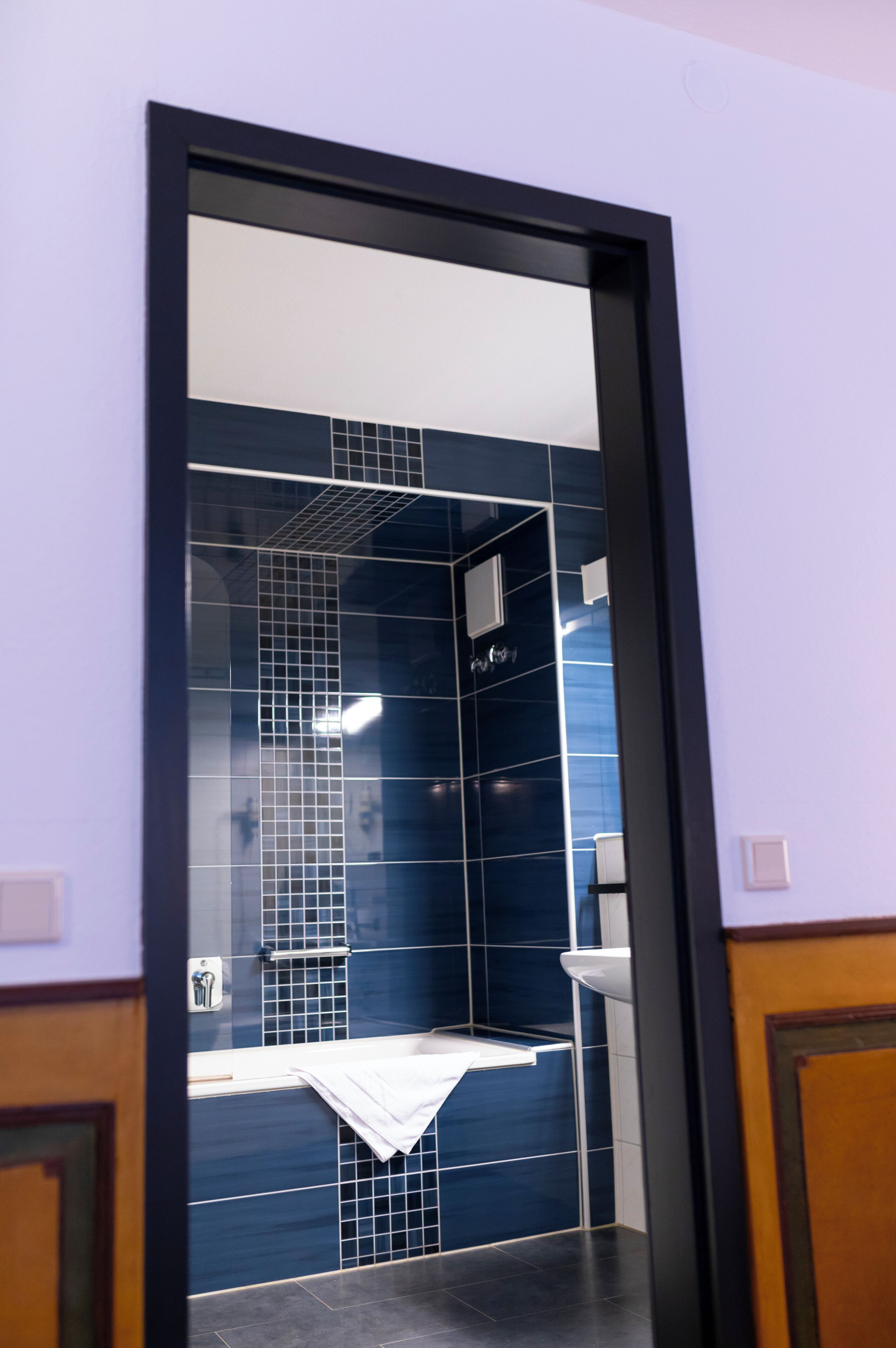 A bathroom with a blue-tiled wall, a white sink, and a towel hanging on the wall.