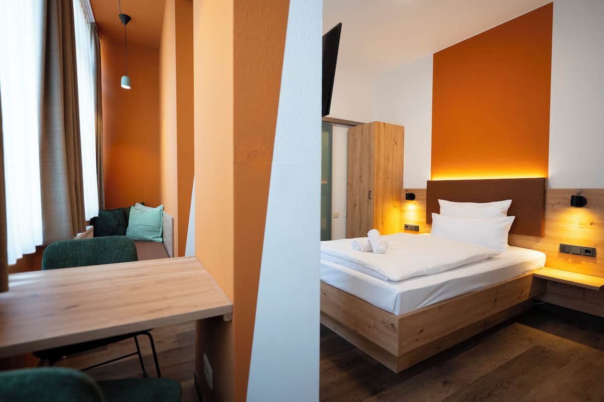 Una habitación de hotel moderna con una cama de madera, un escritorio y una zona de estar con vistas al exterior.