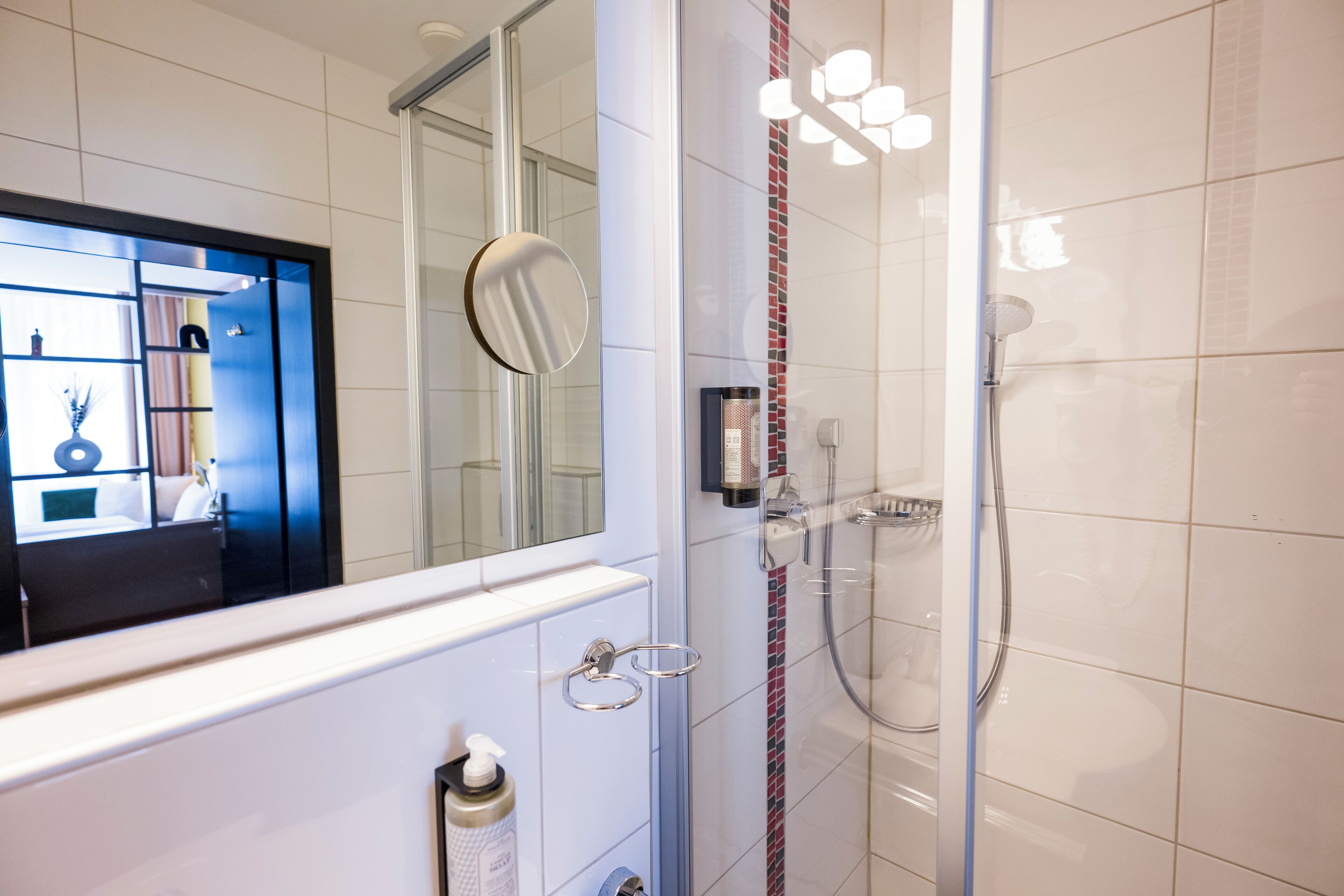 Une salle de bain moderne avec une douche à l’italienne en verre, un miroir et un mur recouvert de carreaux blancs.