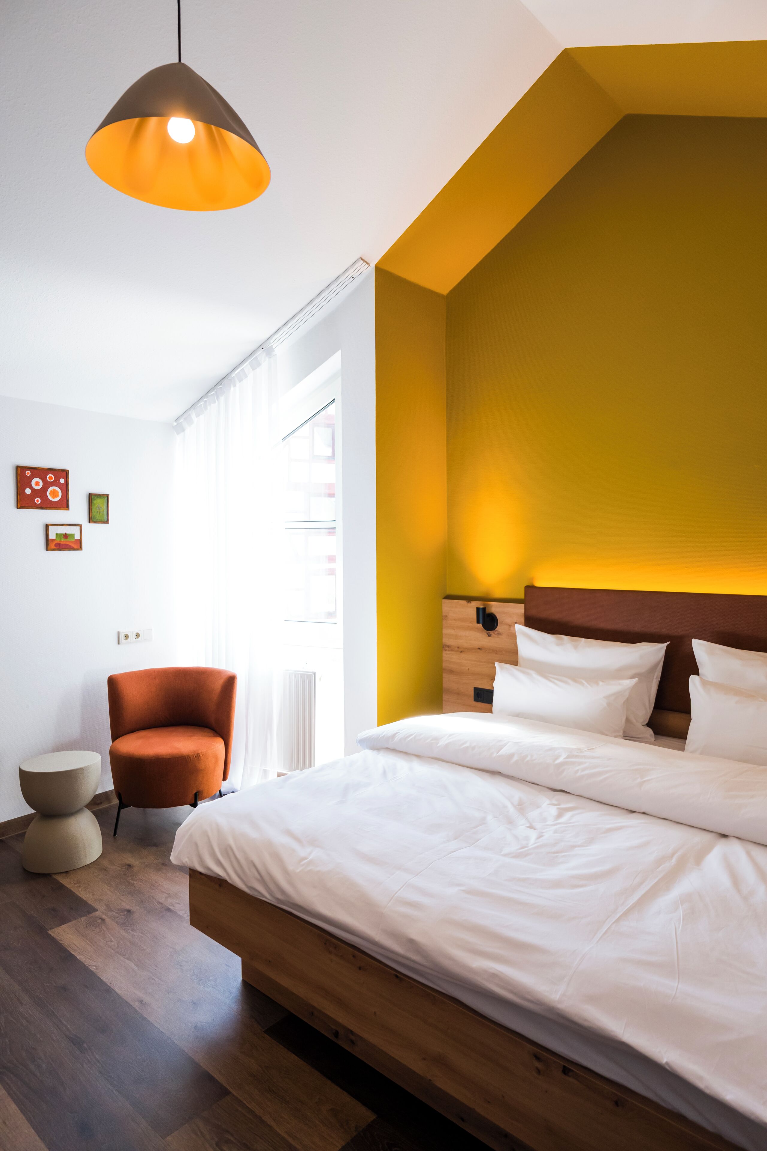 Ein modernes Schlafzimmer mit einem Holzbett, einem braunen Sessel und einer Pendelleuchte.