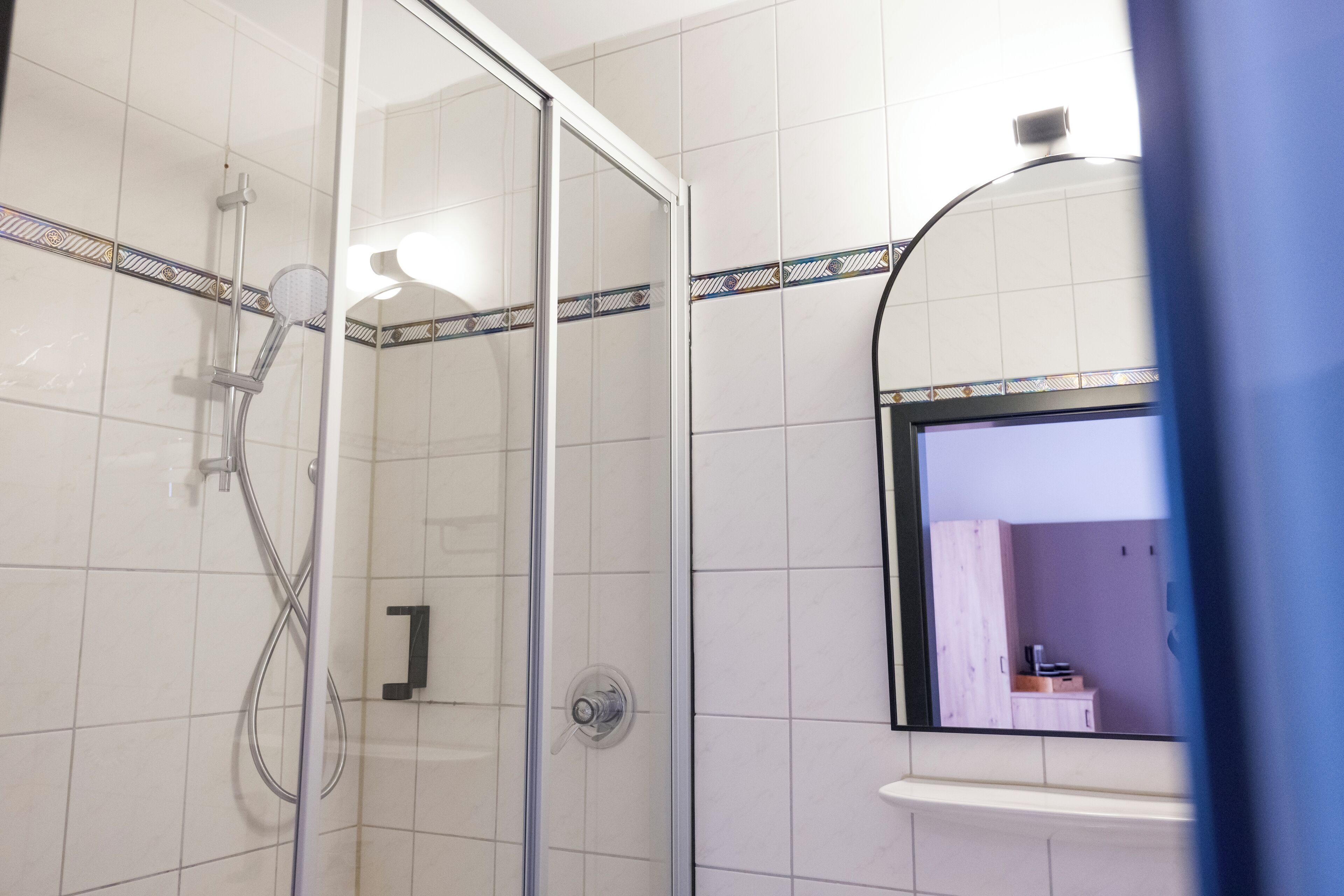 A glass-enclosed shower with a handheld showerhead and a wall-mounted faucet.