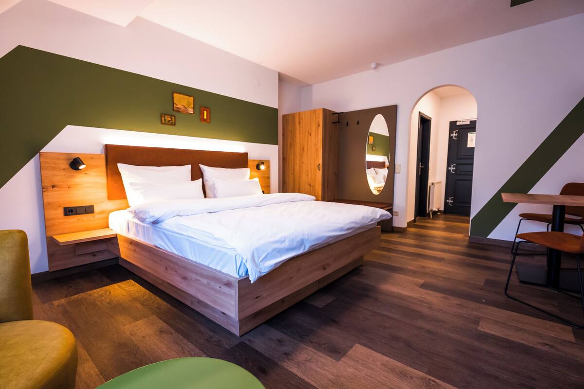 Un dormitorio moderno con una cama de madera, una pared de acento verde y una zona de comedor con mesa y sillas.