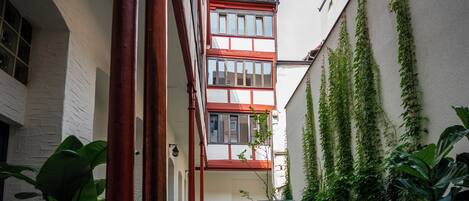 A narrow courtyard with a red-brick building, potted plants, and a tiled floor.
