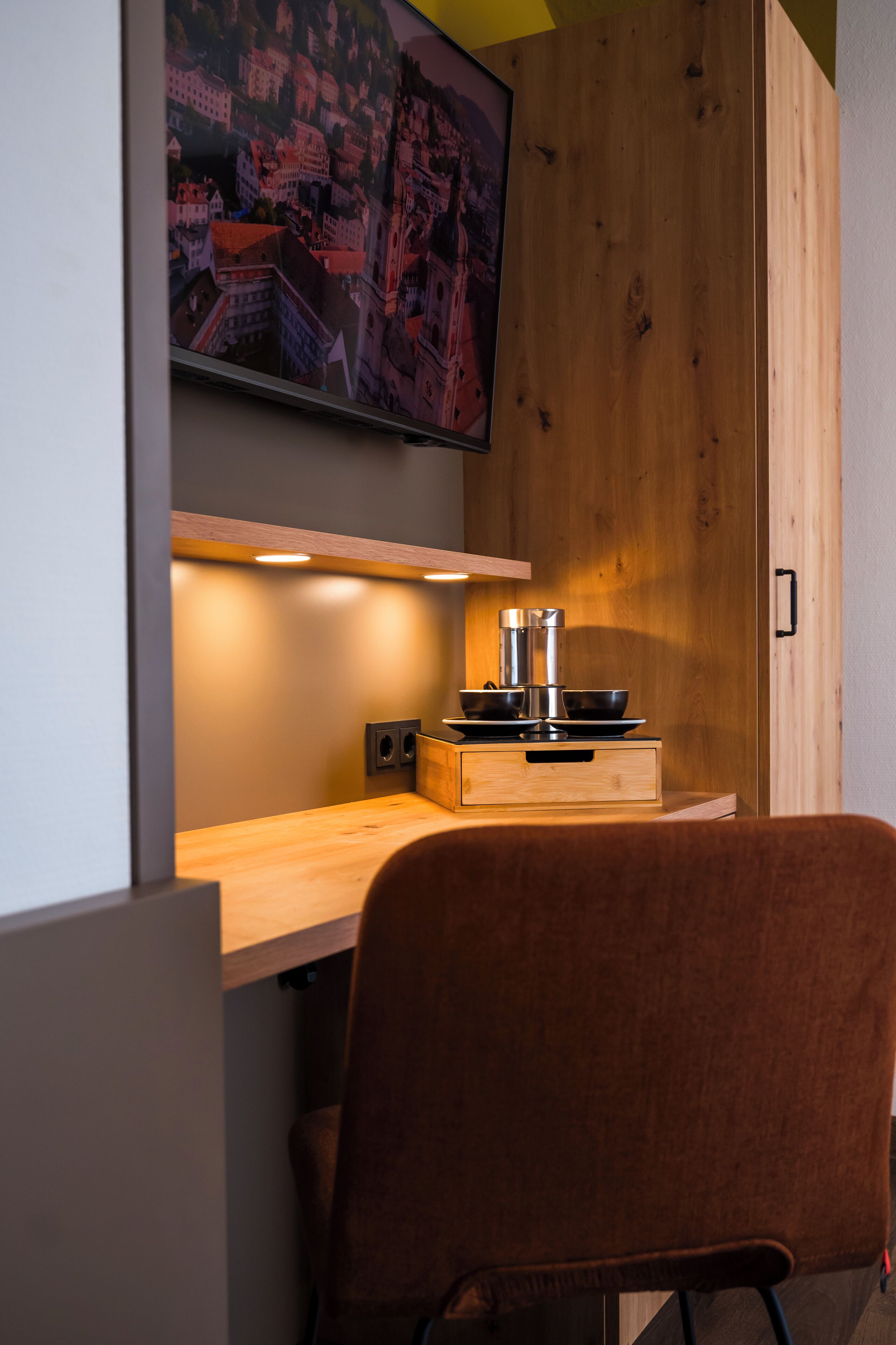 A modern kitchen with wooden cabinetry, a built-in stove, and a television mounted on the wall.
