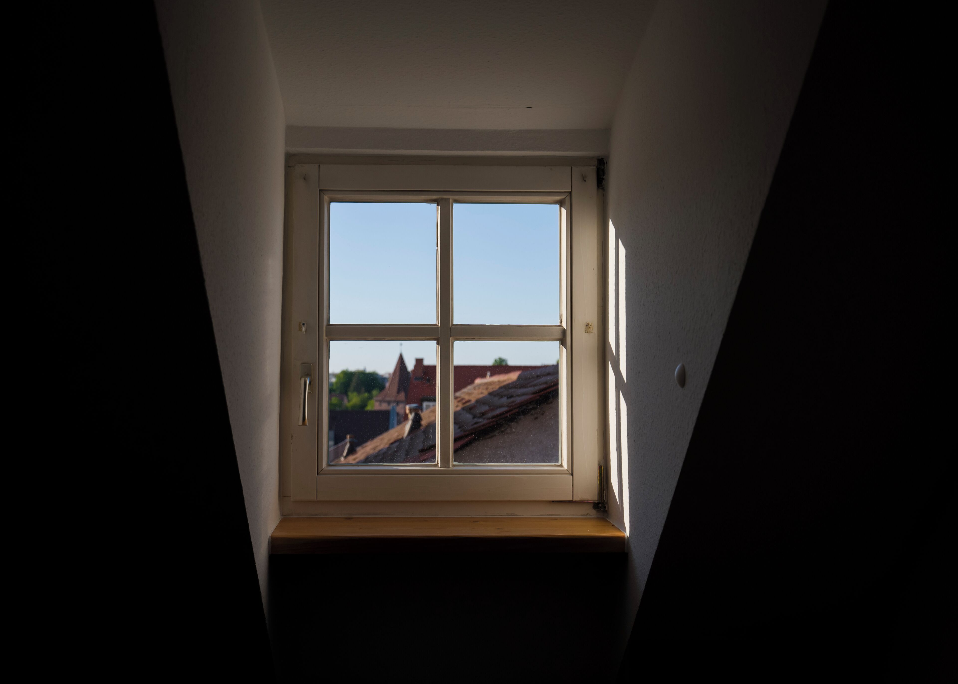 A dormer window with a view of rooftops and a clear sky.