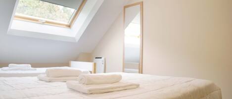 Une chambre avec un puits de lumière, un lit avec des serviettes soigneusement pliées, une table de chevet et un miroir au mur.