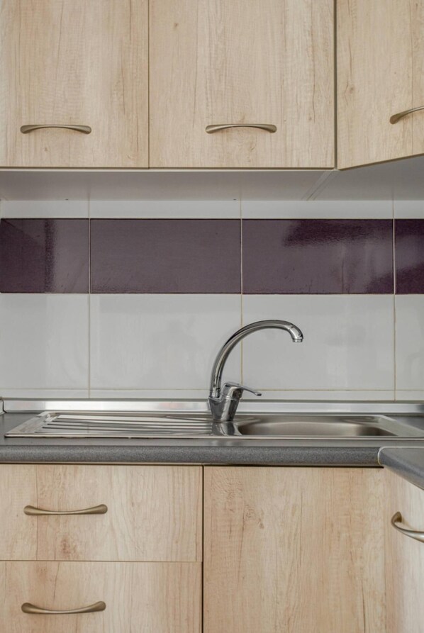 Una cocina con armarios de madera clara, un lavamanos de acero inoxidable y un salpicadero blanco y negro.