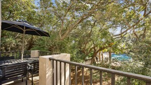 Un espace extérieur aménagé avec une table et des chaises, un parasol et une vue sur une piscine entourée d’arbres.
