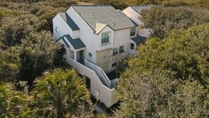 Une maison à deux étages, dotée d’un toit en pente et entourée d’une végétation luxuriante.