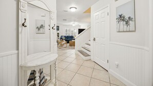 Un couloir aux murs blancs, avec une porte blanche, une console blanche et un escalier menant à une autre pièce.