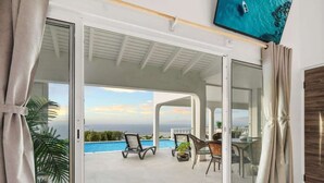 Une chambre moderne dotée d’une porte-fenêtre coulissante donnant sur une piscine, d’un téléviseur à écran plat fixé au mur et offrant une vue sur l’océan.