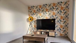A living room with a flat-screen TV, a coffee table, a sofa, and a floor lamp. - New, comfortable bungalow (Les Pieux)