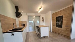 A modern kitchen with a built-in oven, a sink, and a dining area with a table and chairs. - New, comfortable bungalow (Les Pieux)