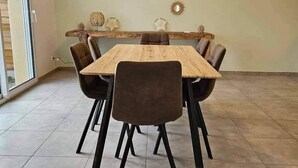 A dining area with a wooden table and six chairs, a decorative ceiling light, and wall-mounted sunburst mirrors. - New, comfortable bungalow (Les Pieux)