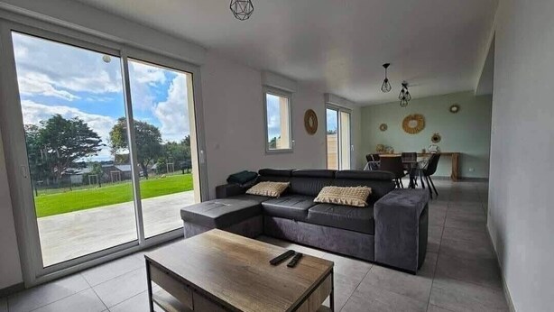 A modern living room with a sectional sofa, a wooden coffee table, and a dining area in the background. - New, comfortable bungalow (Les Pieux)