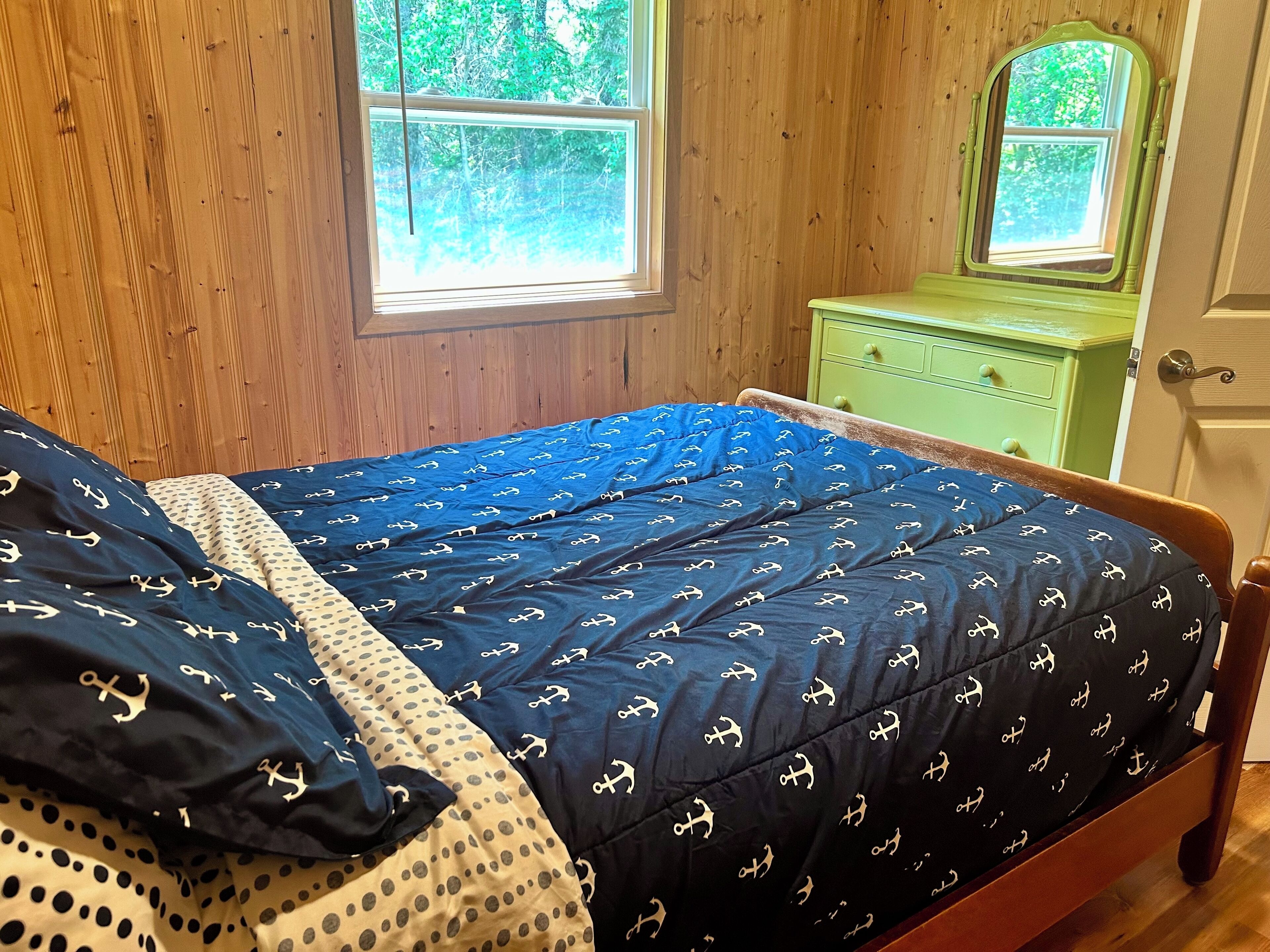 A wooden-paneled room with a bed, two windows, and a green dresser.
