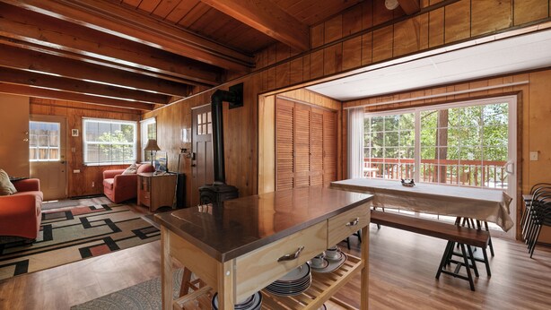 A spacious kitchen with a wooden island, a dining area with a table and chairs, and large windows offering a view of the outdoors. - Chateau Rouge (Big Bear Lake)