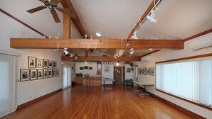 A spacious room with wooden floors, a high ceiling with exposed beams, and a kitchen area in the center.