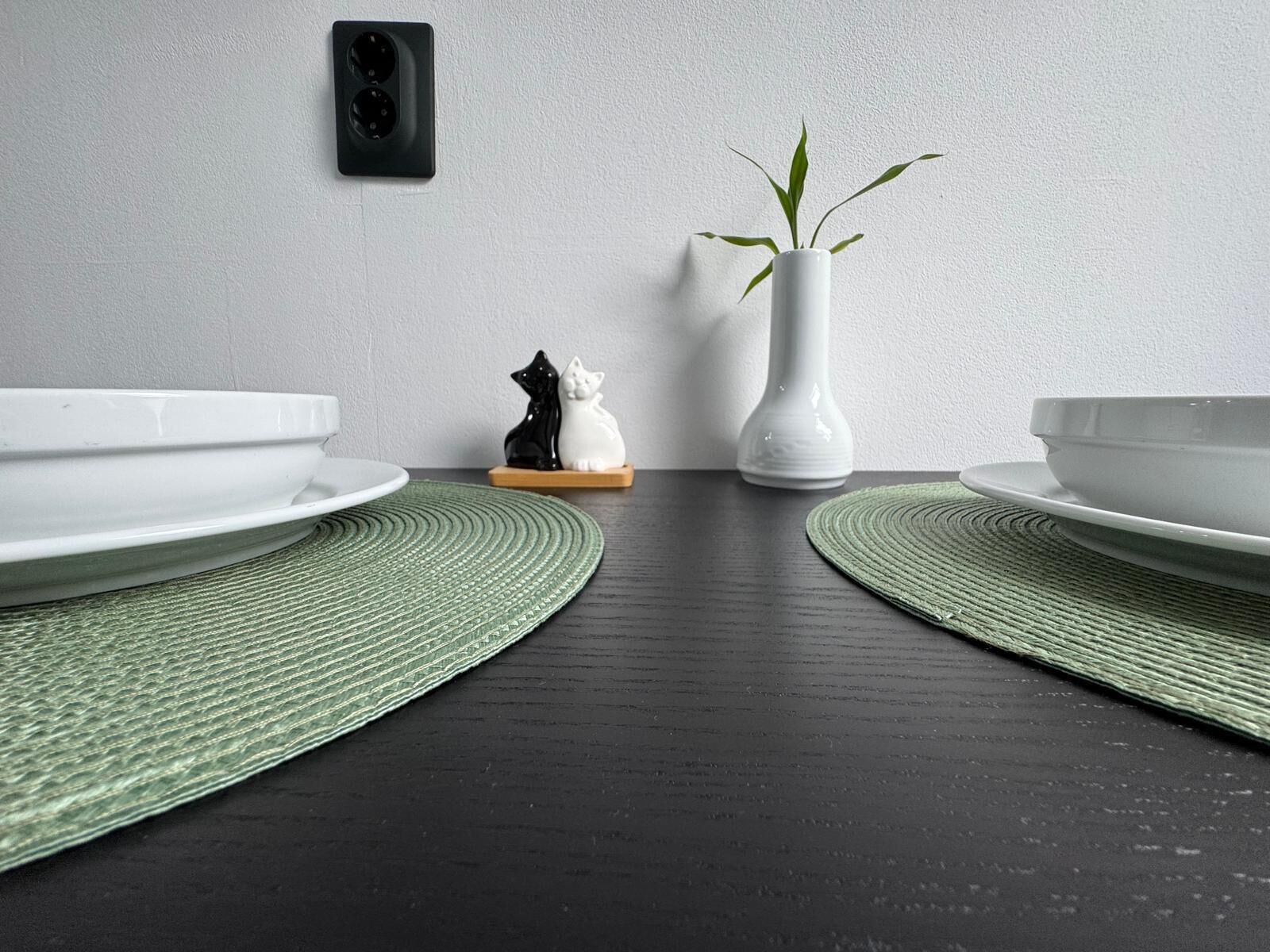Casa de banho moderna com duas pias, um vaso branco com uma planta e uma figurina de gato preto e branco numa prateleira de madeira.