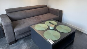 Una sala de estar moderna con un sofá gris, una mesa de centro negra con individuales verdes, y un control remoto sobre la mesa.