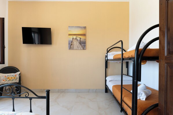 A room with bunk beds, a flat-screen TV, and a painting of a sunset over a pier. - Appartamento Cala Pescatori (Villanova)