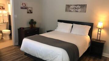 A neatly arranged bedroom with a bed, bedside tables, a nightstand, a wall-mounted sign, and a bathroom visible through an open door.