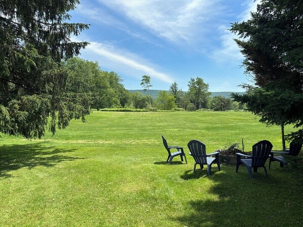A grassy outdoor area with several Adirondack chairs arranged in a semi-circle. - Charming 2-bedroom cottage with AC, WiFi, 4 mi to Cooperstown Dreams Park (Milford)