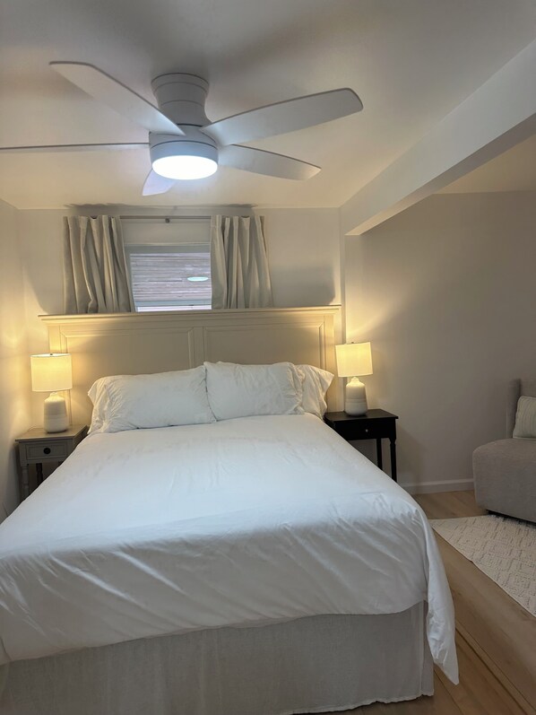 A neatly made bed with white linens, two bedside lamps, a ceiling fan, and a window with curtains. - Charming 2-bedroom cottage with AC, WiFi, 4 mi to Cooperstown Dreams Park (Milford)