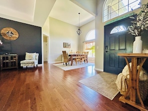 A spacious living room with hardwood flooring, a dining area with wooden chairs, a large window, and a dark blue door. - The Chick-Inn: Monthly Discounts, Groups, Parking! (Southport)