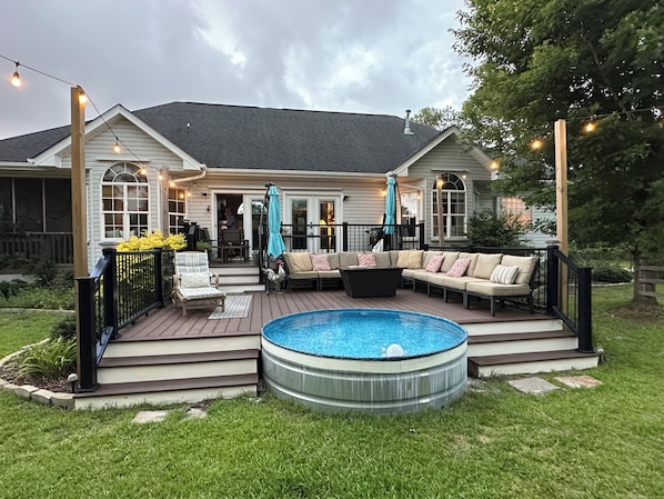 A deck with a hot tub, outdoor furniture, and string lights. - The Chick-Inn: Monthly Discounts, Groups, Parking! (Southport)
