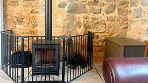 A stone wall, a black fireplace with a chimney, and a red leather bench. - Historic Woodland Getaway, Perfect for Cosy Gatherings - v family-friendly (Kilwinning)