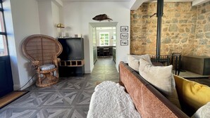 A modern living room with a stone wall, a fireplace, a television, and a wicker chair. - Historic Woodland Getaway, Perfect for Cosy Gatherings - v family-friendly (Kilwinning)