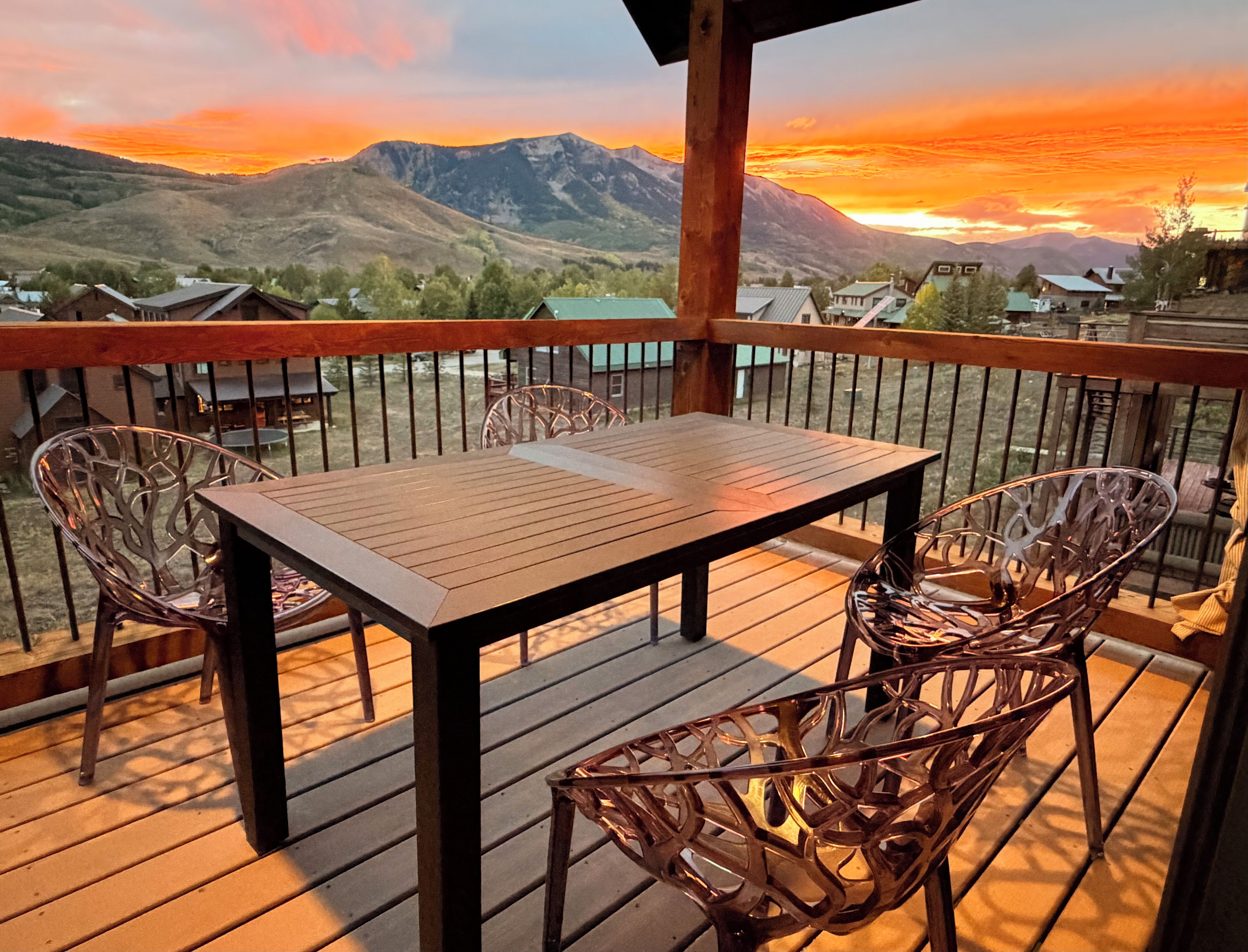 Eine Holzterrasse mit Tisch und Stühlen, mit Blick auf eine gebirgige Landschaft.
