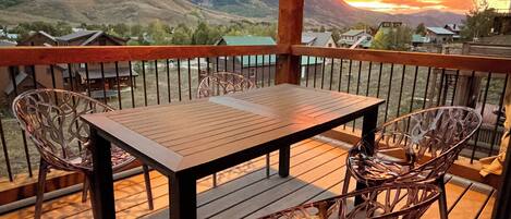 Eine Holzterrasse mit Tisch und Stühlen, mit Blick auf eine gebirgige Landschaft.