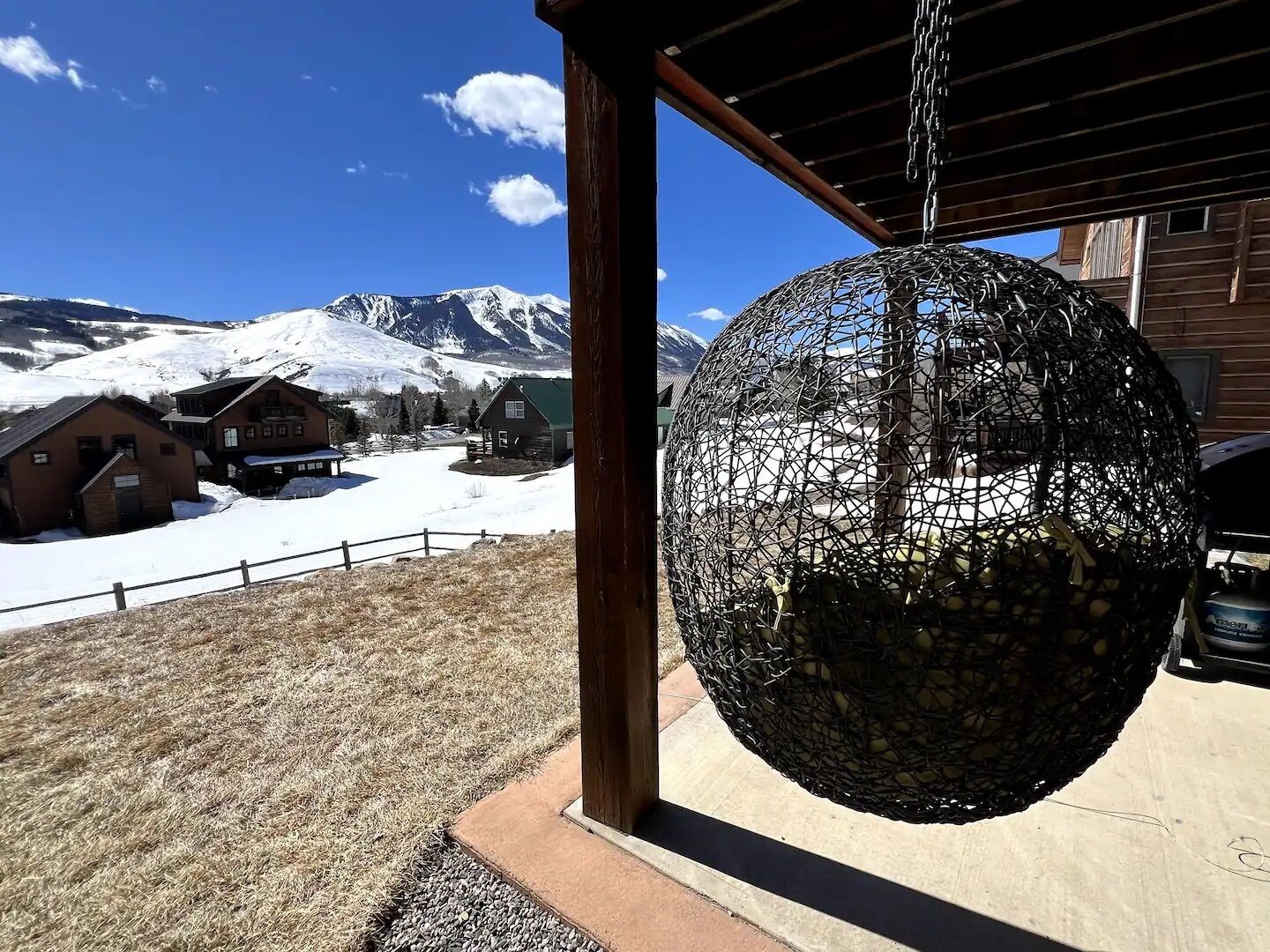 A spherical hanging object, possibly a decorative item, in a covered outdoor area with a view of snow-covered mountains and wooden buildings in the background.