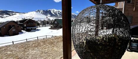 A spherical hanging object, possibly a decorative item, in a covered outdoor area with a view of snow-covered mountains and wooden buildings in the background.