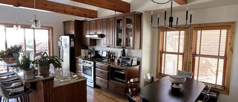 A spacious kitchen with wooden beams, a dining area with a table and chairs, and large windows providing natural light.