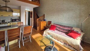 Una sala de estar acogedora con un sofá, una mesa de centro de vidrio y un comedor con sillas, y una cocina al fondo.