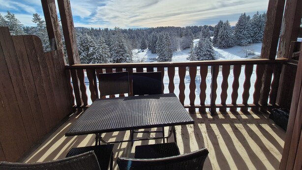 Una terraza de madera con una mesa y sillas, con vista a un bosque nevado.