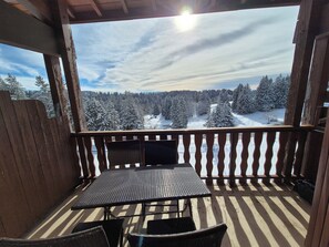 A wooden deck with a table and chairs, overlooking a snowy forest. - Duplex at the Foot of the Slopes – Sleeps 6 (Les Deserts)
