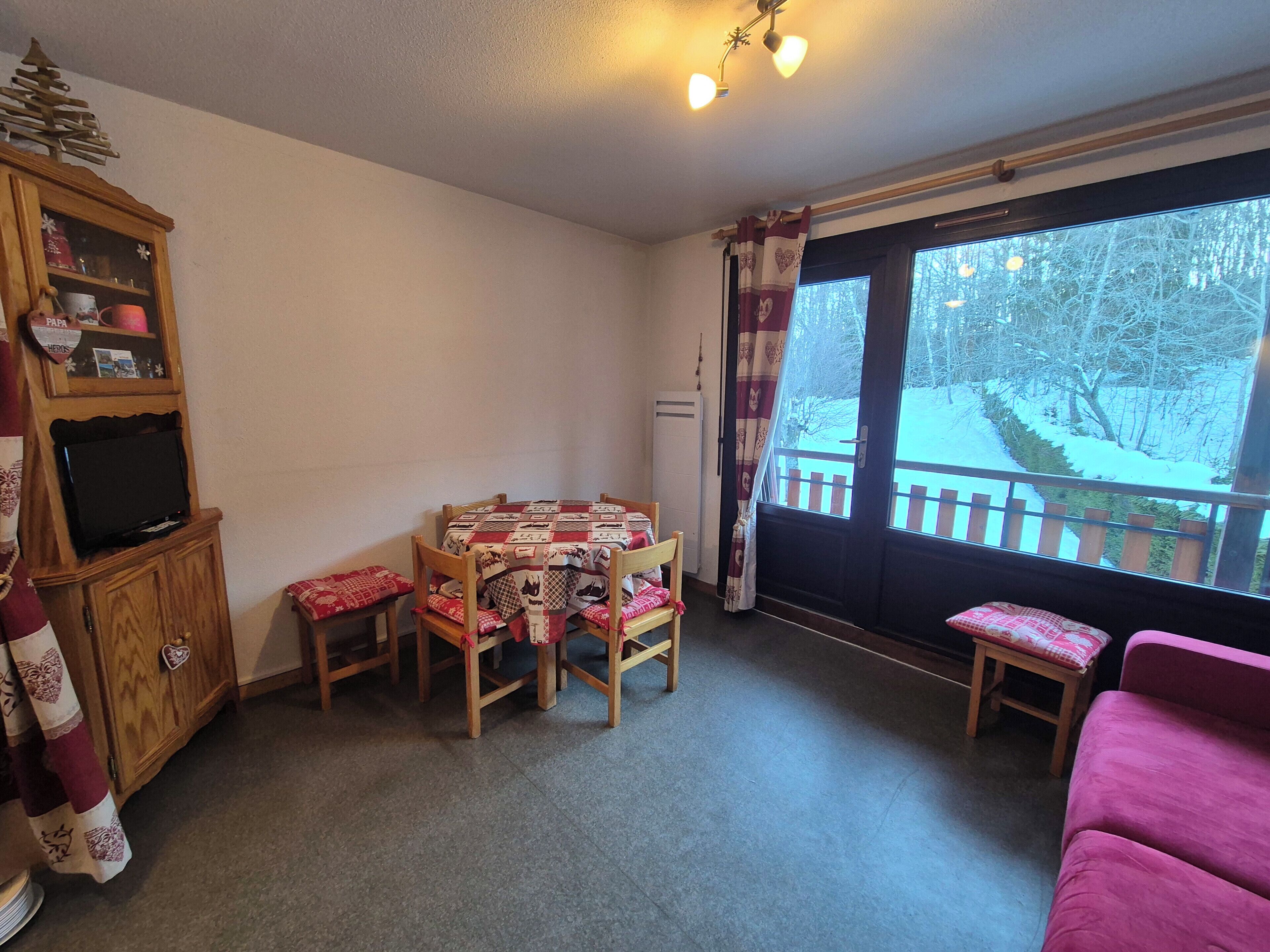Een gezellige woonkamer met een houten tv-meubel, een eettafel met stoelen, een roze bank en uitzicht op een besneeuwde veranda.