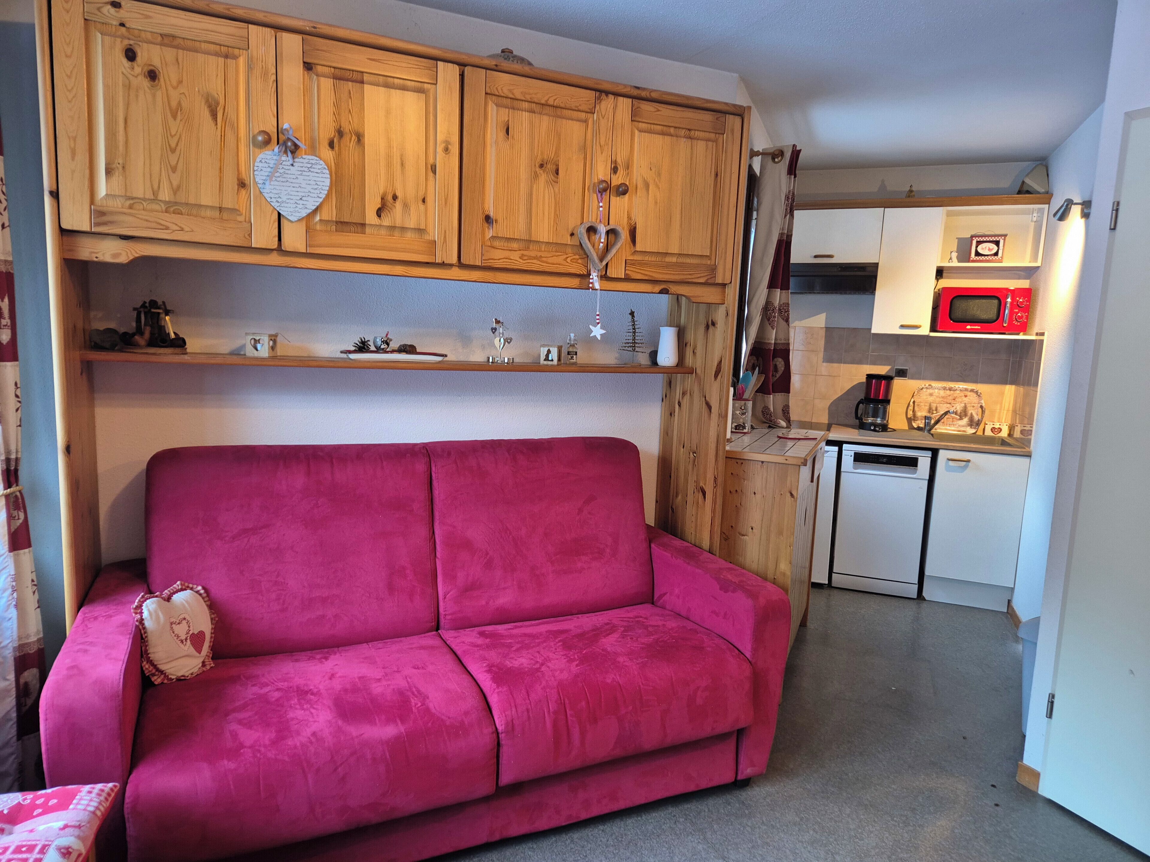A compact kitchen with wooden cabinets, a pink sofa, and a microwave.