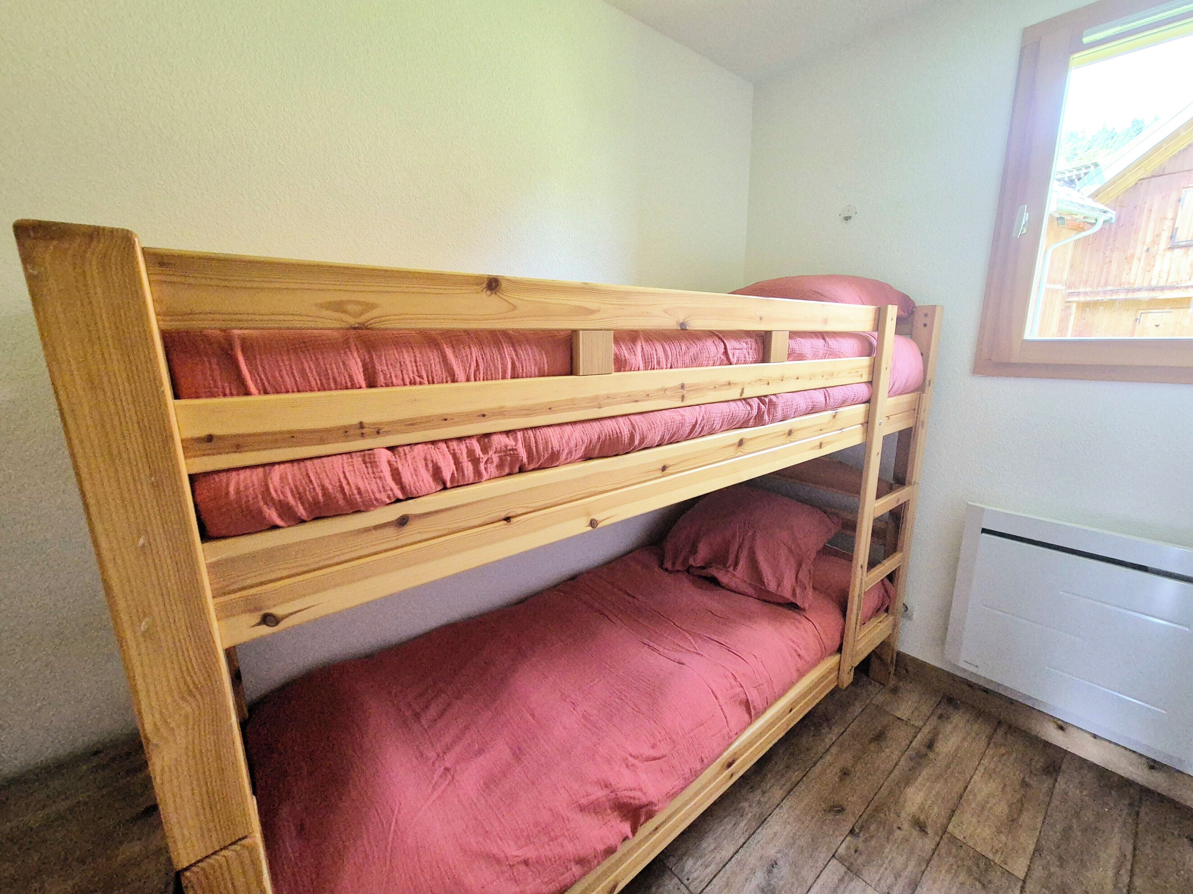 Ein Stockbett mit rosa Bettwäsche in einem Zimmer mit Holzboden und einem weißen Heizkörper.