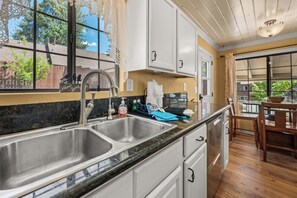 A kitchen with a double sink, a window with lace curtains, and a view of the outdoors. - Chipmunk House (Big Bear Lake)