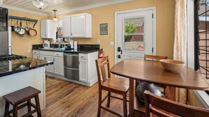 Une cuisine avec des meubles blancs, un fourneau et un coin repas comprenant une table et des chaises en bois.
